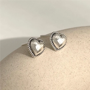 Close-up of 925 sterling silver heart earrings with twisted rope border on beige stone