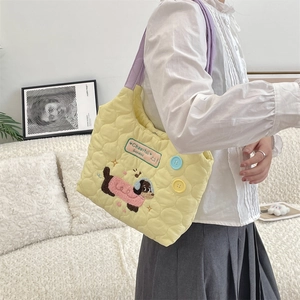 Detalle de bolso acolchado amarillo con asas moradas y bordado de perrito animado