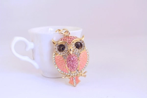 Detail of pink crystal owl keychain with gold plating leaning on a white ceramic cup