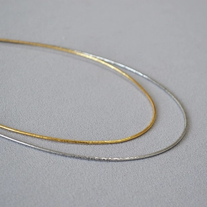 Collane choker minimaliste in oro e argento su tessuto grigio chiaro con riflessi