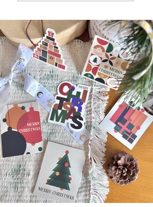 Flat lay of Christmas gift tags and stickers with pine cones on a cream woven rug