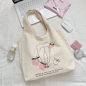 Detail of canvas tote bag with peach illustration and inspirational quote beside a laptop