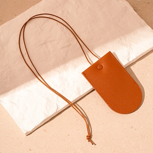 Detail view of the brown leather neck strap pouch with snap closure on a stone display