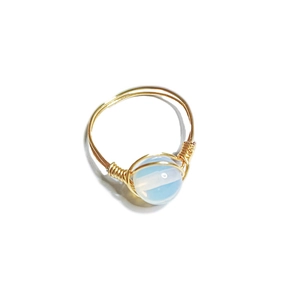 Macro view of handmade gold wire-wrapped ring with a translucent light blue opal bead