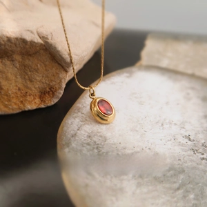 Macro shot of a vintage gold titanium necklace with a red zircon oval pendant set in bezel
