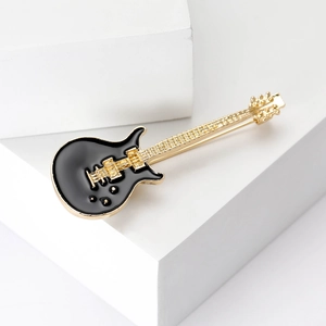 Detail of a black enamel guitar brooch with gold accents on white geometric stands