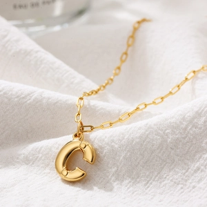 Macro view of gold puffy letter C necklace pendant on white fabric background