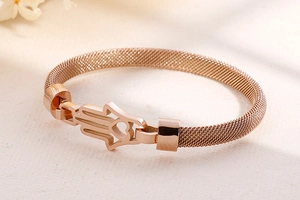 Détail d'un bracelet en maille or rose avec breloques main de Hamsa et petit cœur