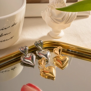 Detailed view of layered heart drop earrings in gold and silver finish on mirror