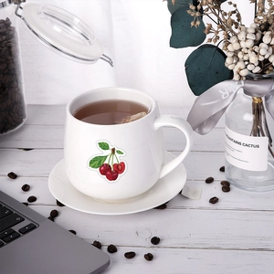 Tazza da caffè in ceramica con ciliegie e piattino su scrivania con chicchi di caffè
