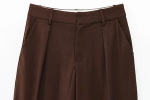 Detail of high-waisted dark brown trousers featuring belt loops and front pleat accents