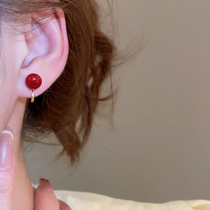 Close-up of a model wearing a gold clip-on earring with a round red pearl bead