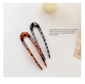 Detail of two resin U-shaped hairpins in amber and grey leopard print patterns