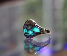 Gothic skull ring featuring luminous blue-green glowing eyes in dark environment