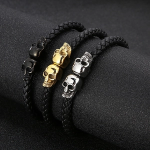 Three braided leather bracelets with skull charms in black, gold, and silver finishes