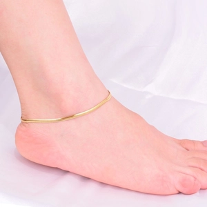 Elegant gold flat snake chain anklet for women shown on model ankle against white silk
