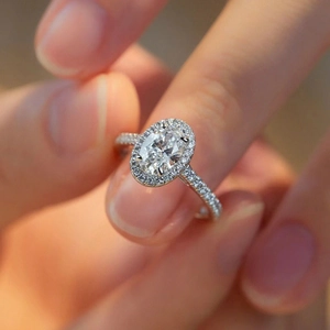 Detailed view of an oval-cut shimmering moissanite ring held by hand with paved band
