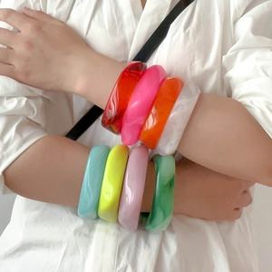 Stack of thick colorful acrylic resin bangles in multiple vibrant shades on a wrist