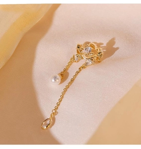 Detail of gold tassel ear cuff with pearls and zircons on beige silk fabric