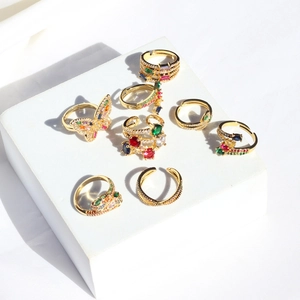 Rainbow gemstone ring set with butterfly and snake designs on white geometric display
