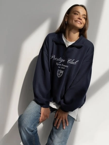 Detail of navy blue half-zip sweatshirt with Prestige Club print and shield logo