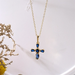 Détail macro du pendentif croix dorée orné de zircons bleus ovales incrustés
