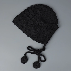 Détail du bonnet en crochet noir fait main avec motifs ajourés et liens à pompons