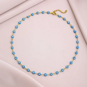 Detailed shot of golden evil eye necklace with blue beads on soft pink fabric background