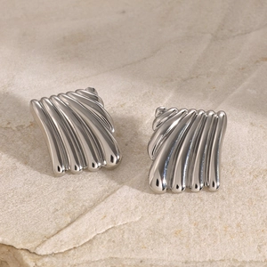 Macro shot of silver square earrings with vertical wavy texture on stone background