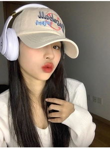 Close-up of beige Baseball Mom embroidered cap worn by a model with headphones
