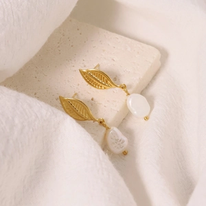 Elegant gold leaf earrings with natural white baroque pearls on a minimalist stone base
