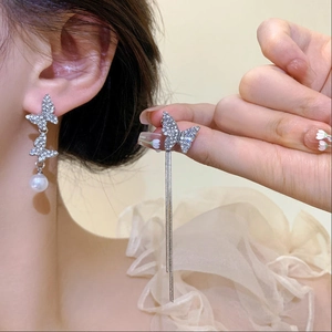 Detailed close-up of asymmetric silver butterfly earrings with pearls and long tassels