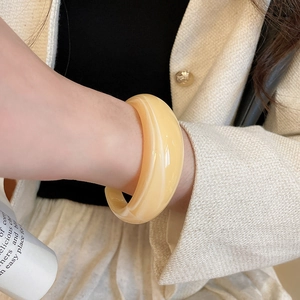 Détail d'un large bracelet en résine crème avec texture marbrée porté avec une veste beige