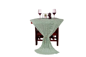 Detail of light green wrinkled gauze table runner draped over a wooden table for weddings
