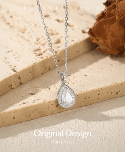 Macro view of pear-shaped moissanite pendant with halo setting on a stone backdrop
