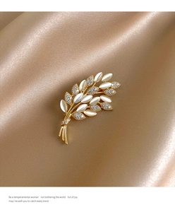 Detailed view of wheat-shaped cat eye brooch with pearls on elegant beige silk fabric