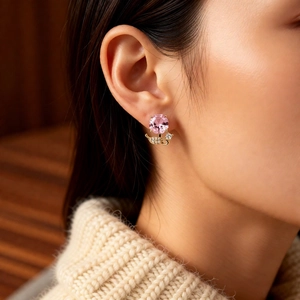 Gros plan d'une boucle d'oreille fleur en cristal rose avec feuilles d'or sur l'oreille