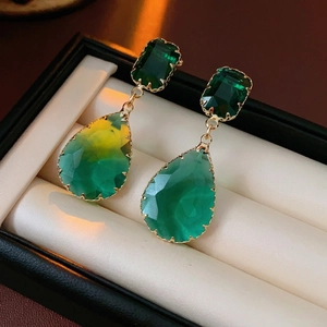 Elegant emerald teardrop earrings with golden metal frames in a luxury jewelry box