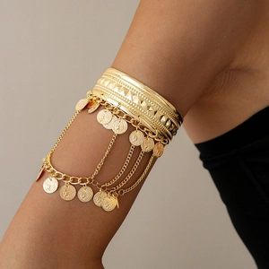 Detail of bohemian gold metal arm cuff with coin pendants and tassel chain on model
