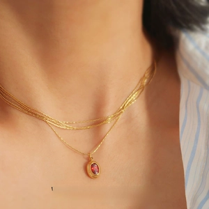 Detail of vintage layered gold necklace with red oval gemstone pendant on model neck