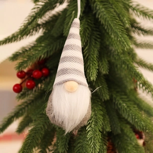 Close-up of a knitted Christmas gnome ornament hanging on a pine tree with berries