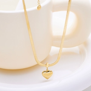 Golden stainless steel heart pendant necklace with flat snake chain on white cup