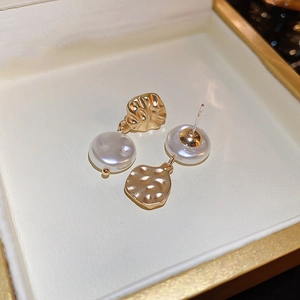 Detail of golden hammered metal earring with white flat round pearl in a jewelry box