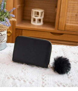 Detail shot of a black quilted leather purse with a fluffy pompom on a lace background