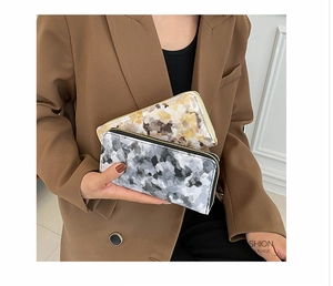 Close-up of long zip-around marble pattern wallets held by a model in a brown suit