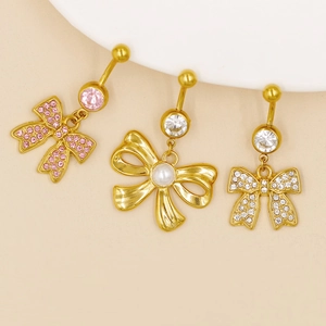 Close-up of gold navel rings featuring bow designs with pink crystals, pearl, and white stones