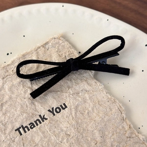 Close-up of black velvet bow hair clip with metal fastener on a minimalist background