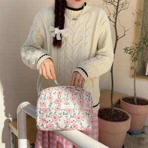 Close-up of a floral quilted cotton makeup bag with zip closure held by a model outdoors