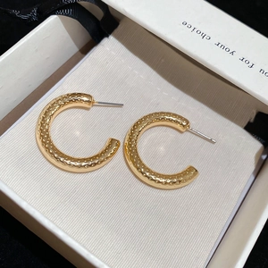 Close-up of golden C-shaped hoop earrings with hammered texture in a jewelry box