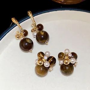 Elegant gold earrings with tiger eye stone and pearls on a beige velvet jewelry tray